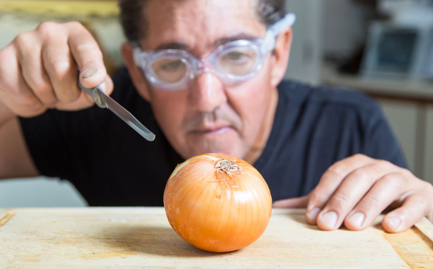Photo shows a man in swmming goggles about to cut into a white onion with a scalpel