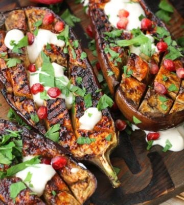 scored vegan miso aubergine steaks topped with parsley, pomegranate, and vegan yogurt