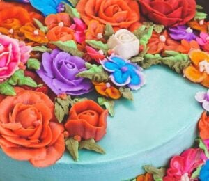 a vegan funfetti cake with vegan icing topped with hand-piped icing flowers in all colors of the rainbow