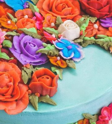 a vegan funfetti cake with vegan icing topped with hand-piped icing flowers in all colors of the rainbow
