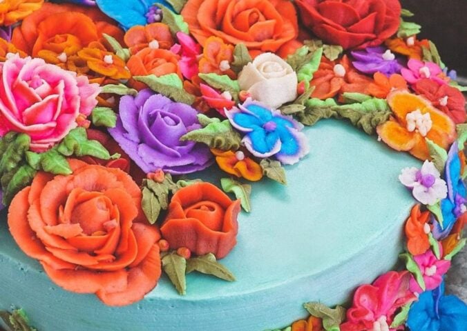 a vegan funfetti cake with vegan icing topped with hand-piped icing flowers in all colors of the rainbow