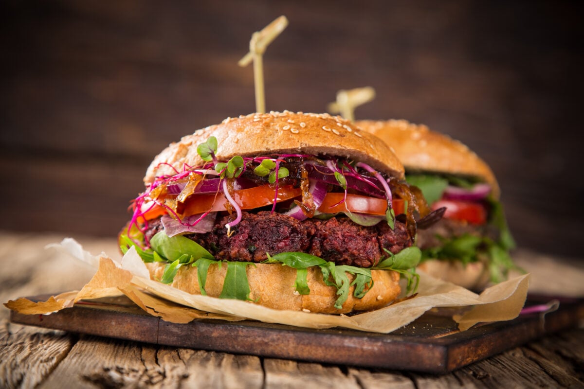 Photo shows two large plant-based burgers on a wooden board