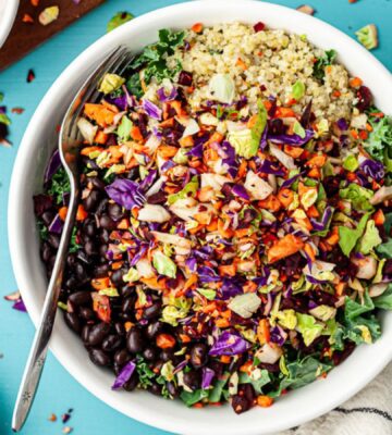 A bowl of brightly colored vegan salad made with a crunchy vegetable-based salad topping