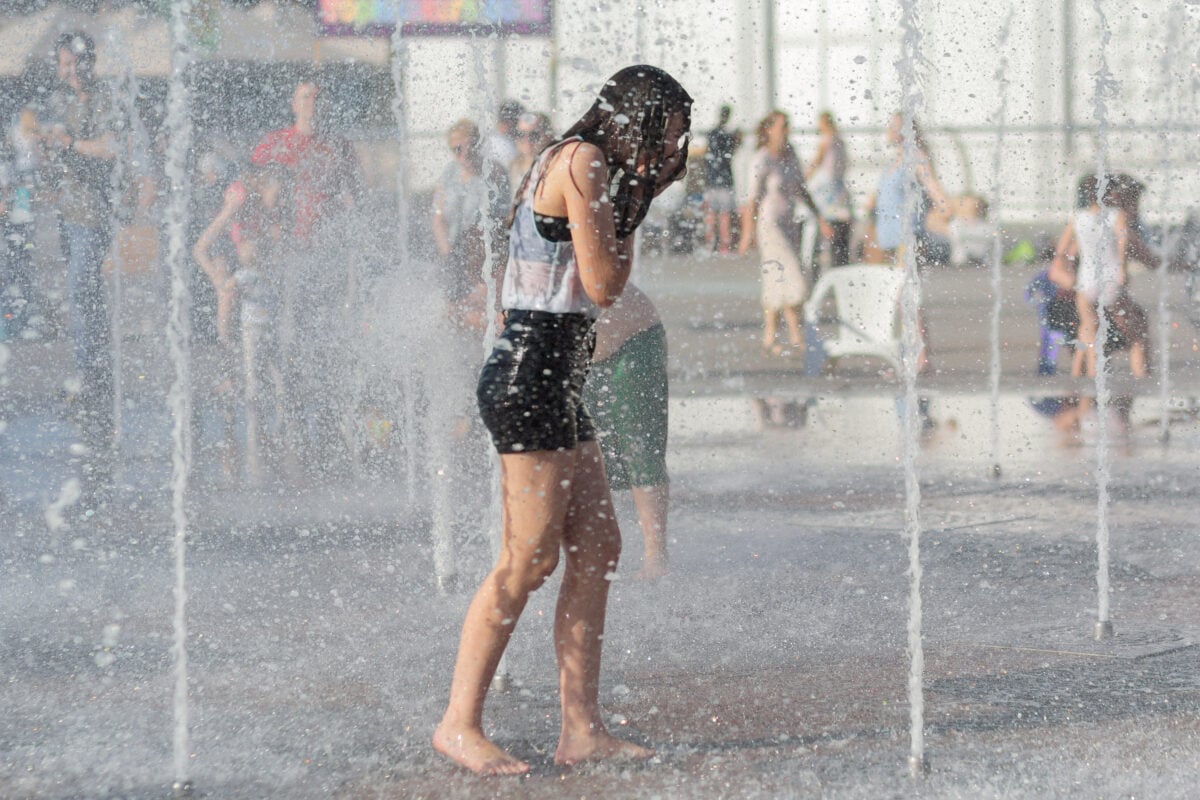 Photo shows a young girl cooling off in some public water fountains