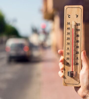 Photo shows someone's hand as they hold up a wooden thermometer on a hot city street - the mercury shows over 40C