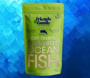 A packet of cat food made from cultivated fish in front of a navy blue patterned background