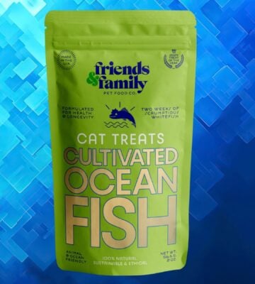 A packet of cat food made from cultivated fish in front of a navy blue patterned background