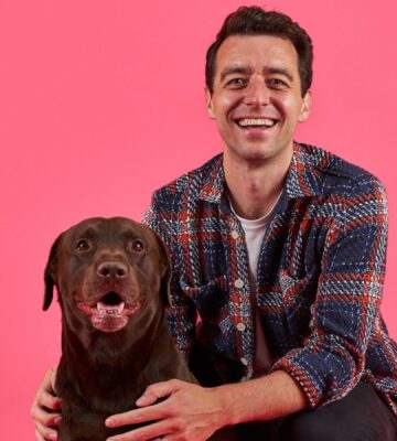 Cultivated meat pet food company Meatly CEO Owen Ensor poses with a brown dog in front of a pink background