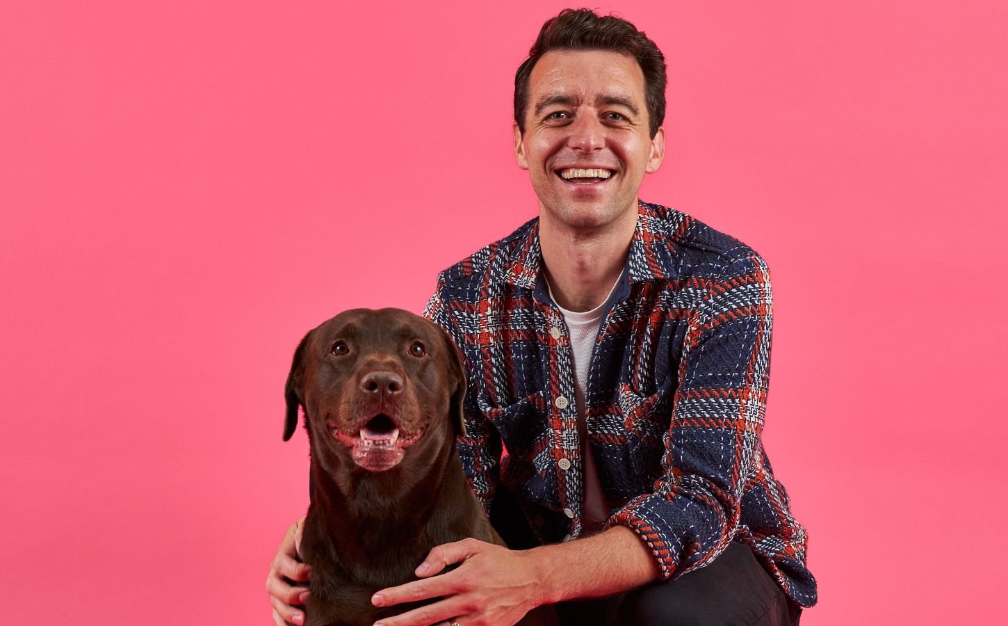 Cultivated meat pet food company Meatly CEO Owen Ensor poses with a brown dog in front of a pink background