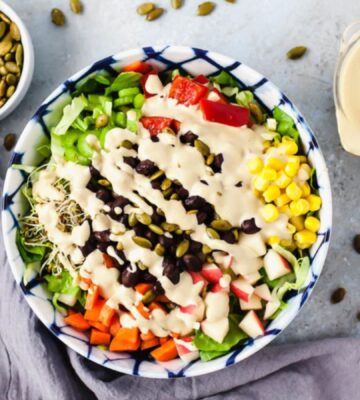 a vegan delicious salad made with lettuce, black beans, corn, vegan Caesar dressing, sprouts, and bell pepper