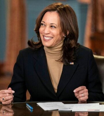 Photo shows Kamala Harris seated at a wooden table and smiling off-camera