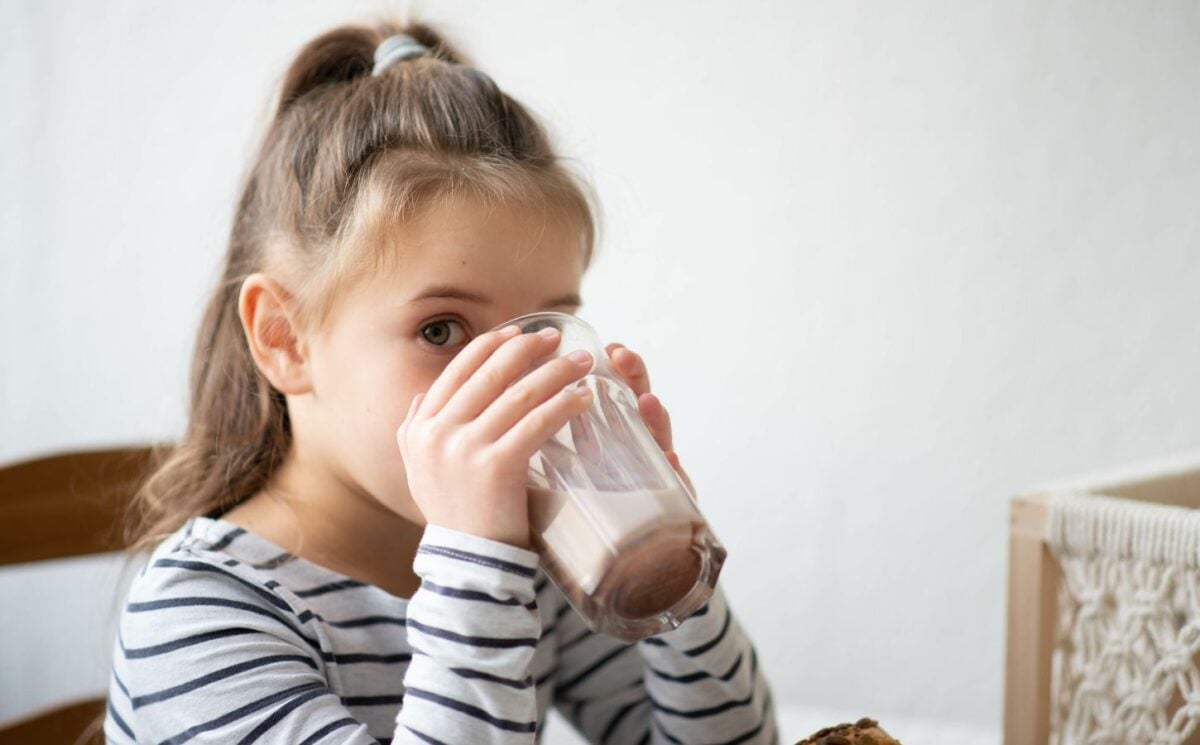 A child drinking a dairy-free protein shake in a kitchen