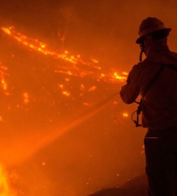 Photo shows the silhouette of a firefighter as they tackle a wildfire at night