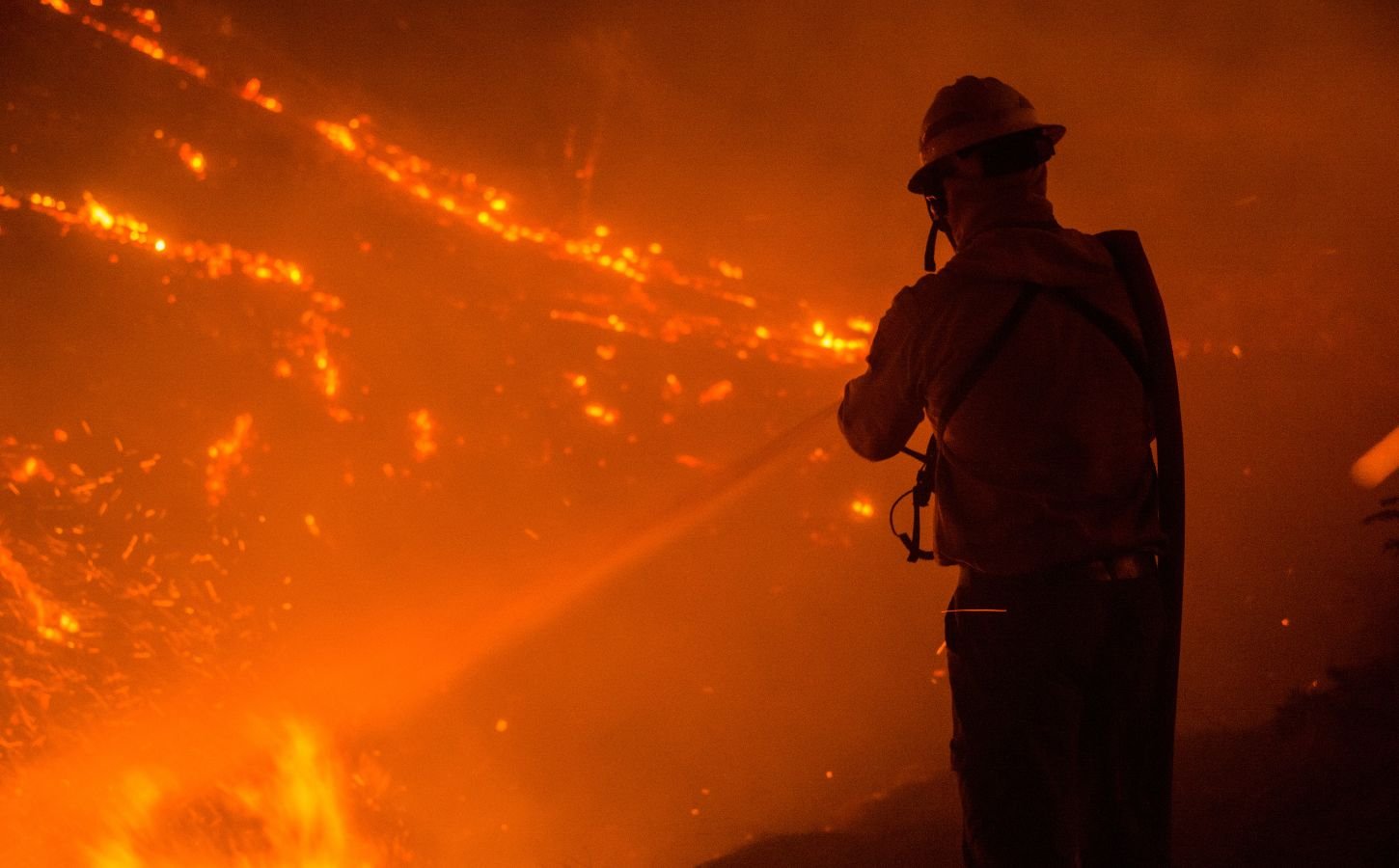 Photo shows the silhouette of a firefighter as they tackle a wildfire at night