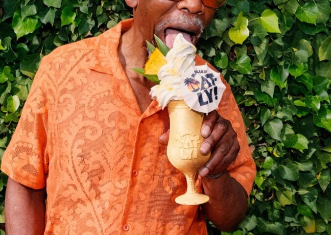 Photo shows a middle-aged Black man in a summery orange shirt holding Oatly and Malibu's new cocktail-inspired alcoholic soft serve, the "Piña Oatlada"
