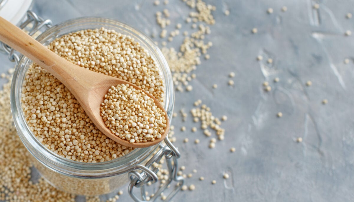 Photo shows a glass dish of dried quinoa with a wooden spoon resting on the top