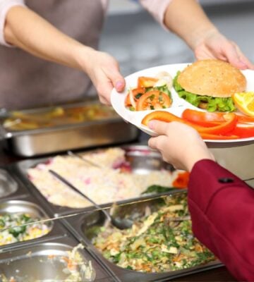 A school lunch worker handing a child a plant-based meal