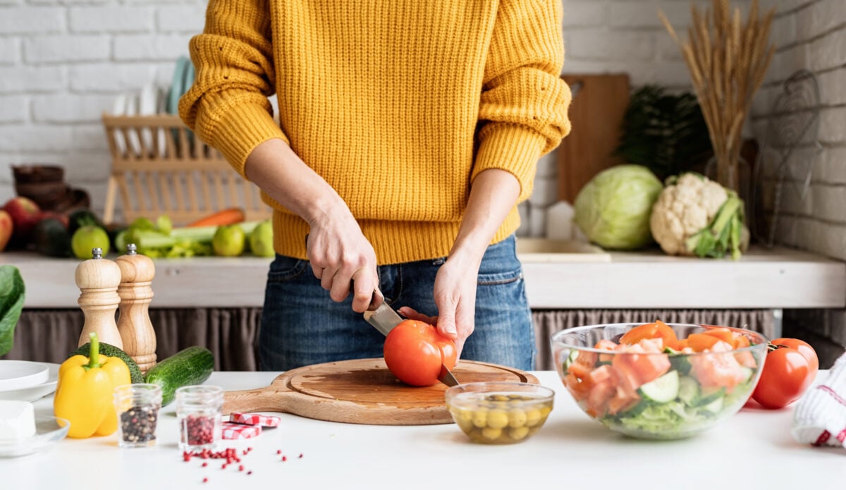 Photo shows a woman cutting fresh vegetables on a kitchen counter