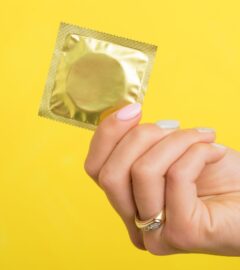 A person holding up a condom in front of a yellow background