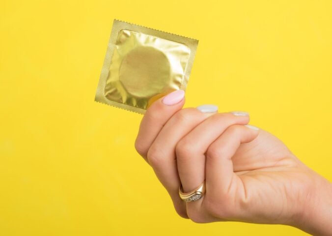 A person holding up a condom in front of a yellow background