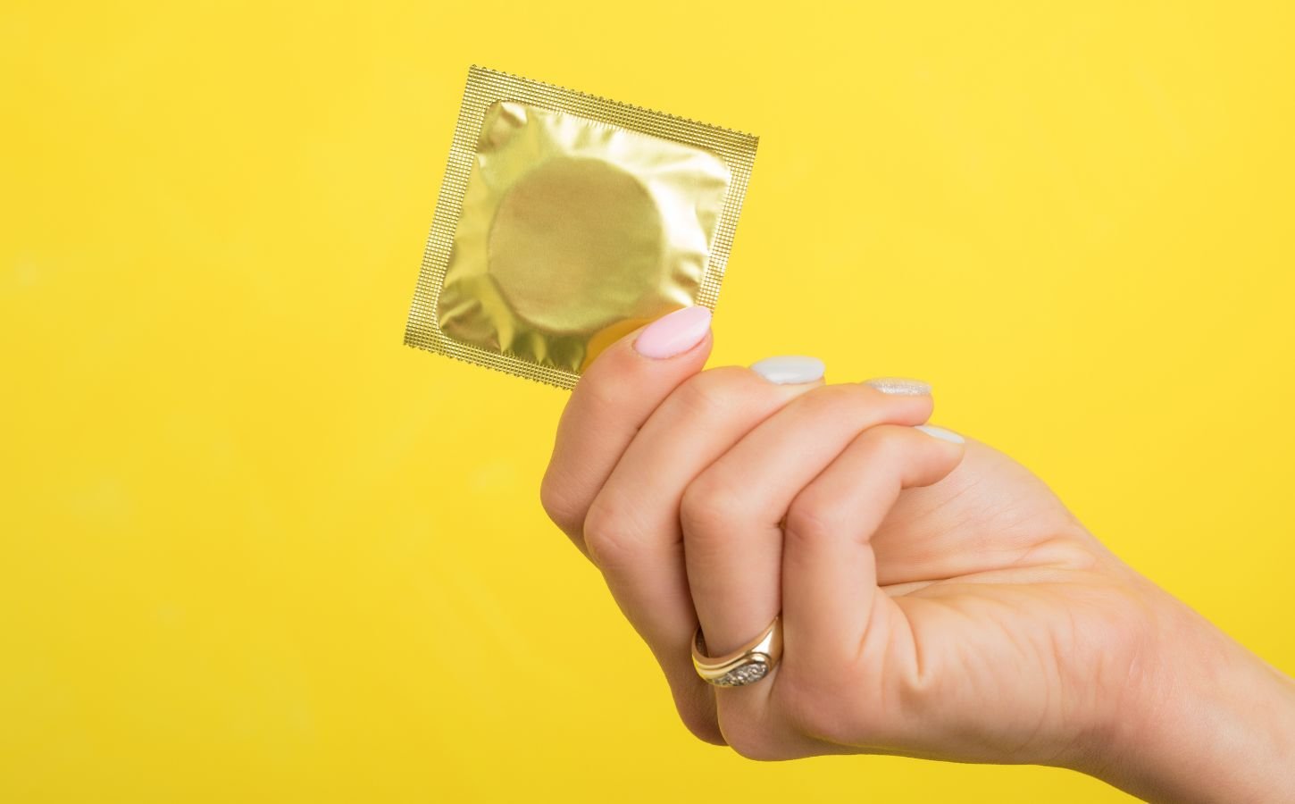 A person holding up a condom in front of a yellow background