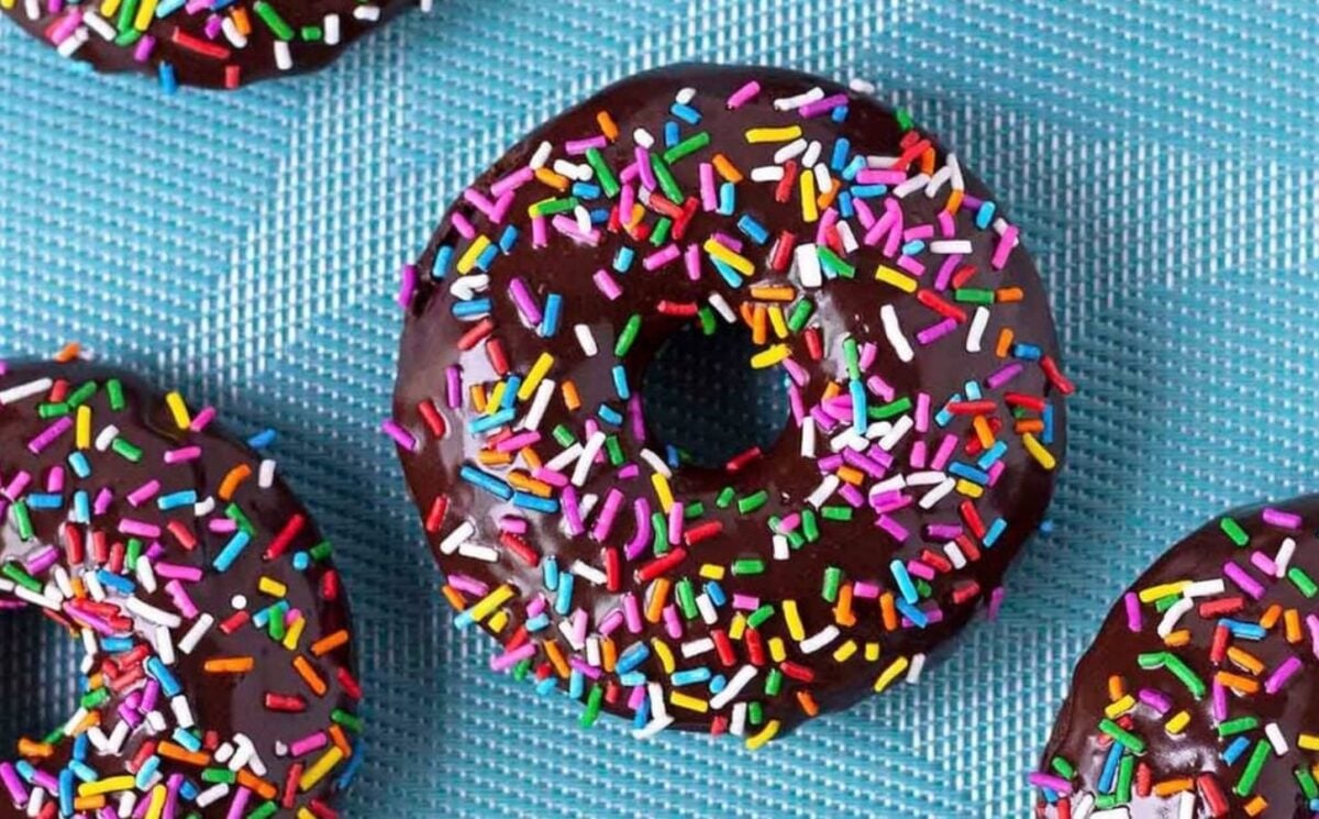 a batch of baked, gluten-free, and vegan chocolate donuts covered in a chocolate glaze and rainbow sprinkles