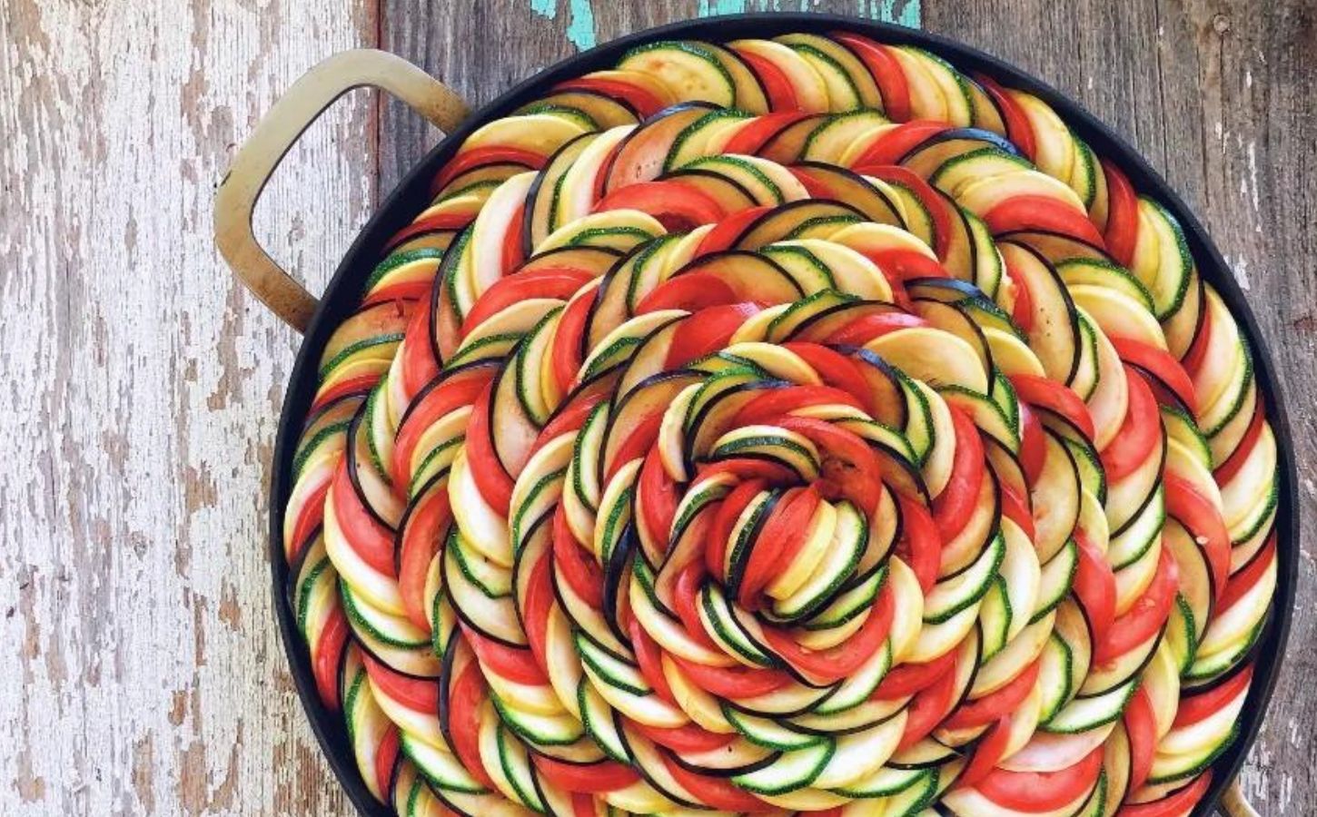 a picture of beautifully arranged ratatouille in colorful spirals of zucchini, tomatoes, pepper, and squash