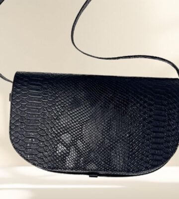 A vegan snake skin leather handbag in front of a beige background