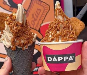 Photo shows two people holding up portions of DÁPPA vegan soft serve together - one in a cone and one in a tub