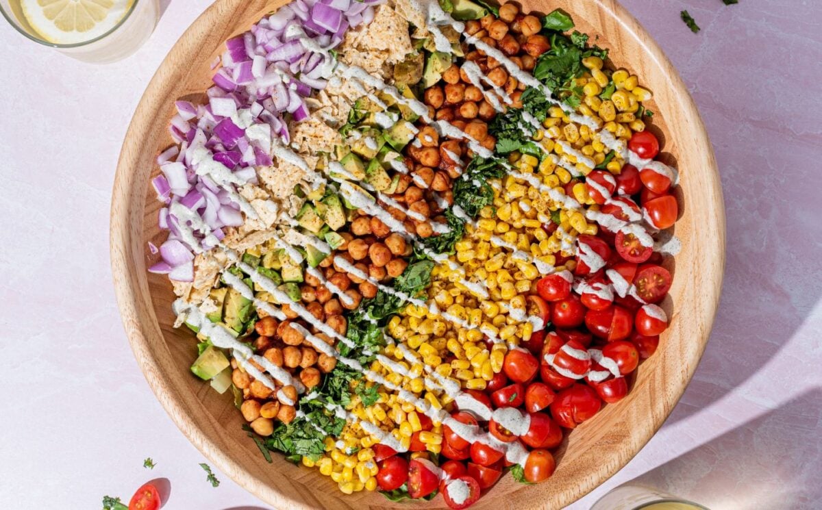 a picture of a beautifully assembled bbq chickpea chopped salad made with a rainbow of vegetables including tomato, corn, chickpeas, lettuce, corn chips, and a hempseed dressing