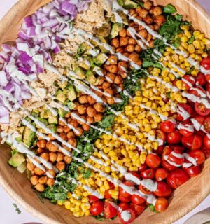 a picture of a beautifully assembled bbq chickpea chopped salad made with a rainbow of vegetables including tomato, corn, chickpeas, lettuce, corn chips, and a hempseed dressing