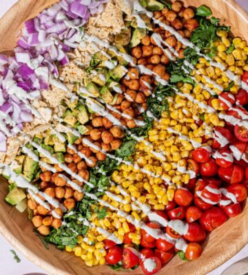 a picture of a beautifully assembled bbq chickpea chopped salad made with a rainbow of vegetables including tomato, corn, chickpeas, lettuce, corn chips, and a hempseed dressing