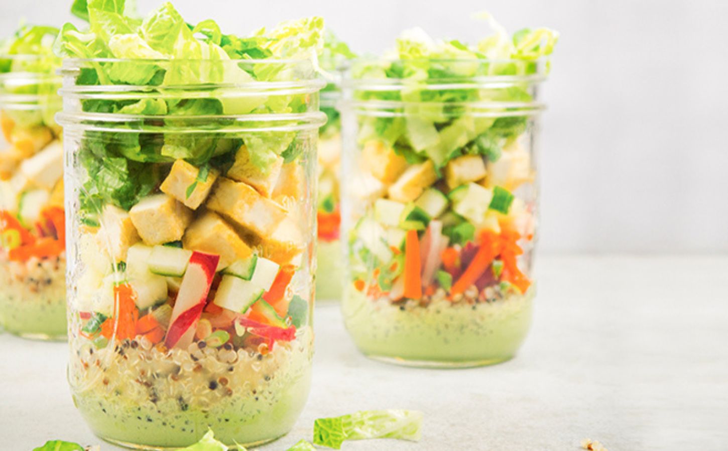 a picture of vegan bahn mi mason jar salads with quinoa, tofu, romaine lettuce, a tasty dressing, and radish