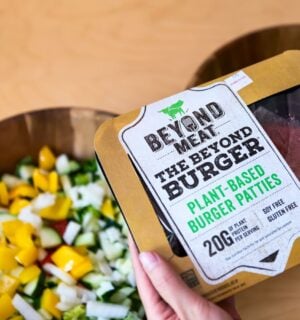 Photo shows someone's hands as they hold up a pack of Beyond Meat burger patties above two bowls of chopped vegetables