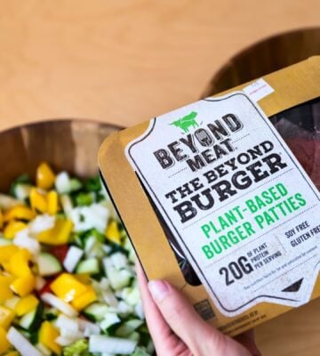 Photo shows someone's hands as they hold up a pack of Beyond Meat burger patties above two bowls of chopped vegetables