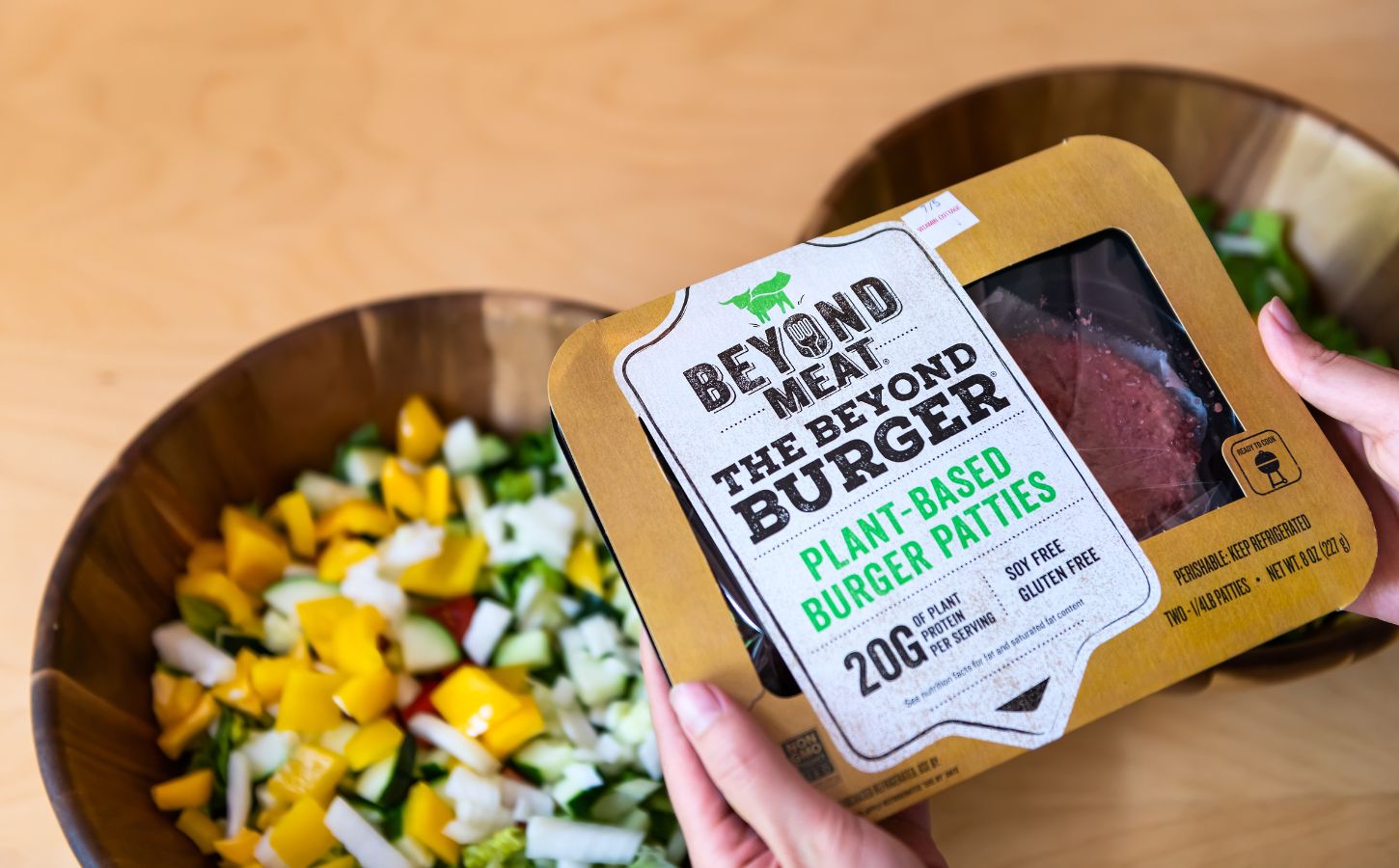 Photo shows someone's hands as they hold up a pack of Beyond Meat burger patties above two bowls of chopped vegetables