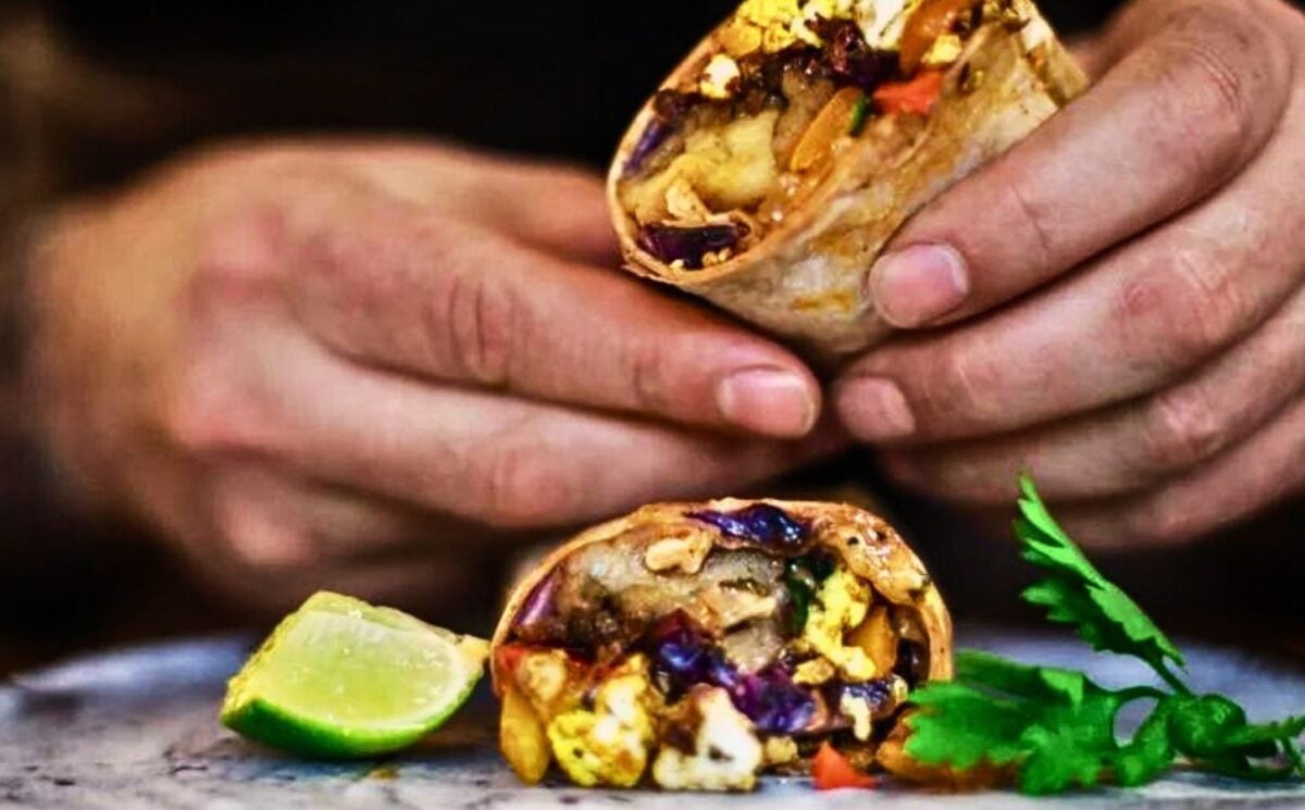 a picture of hands holding an aubergine and tofu scramble breakfast burrito made with harissa, spinach, bell pepper, nutritional yeast, and vegan cheese for a high protein breakfast idea