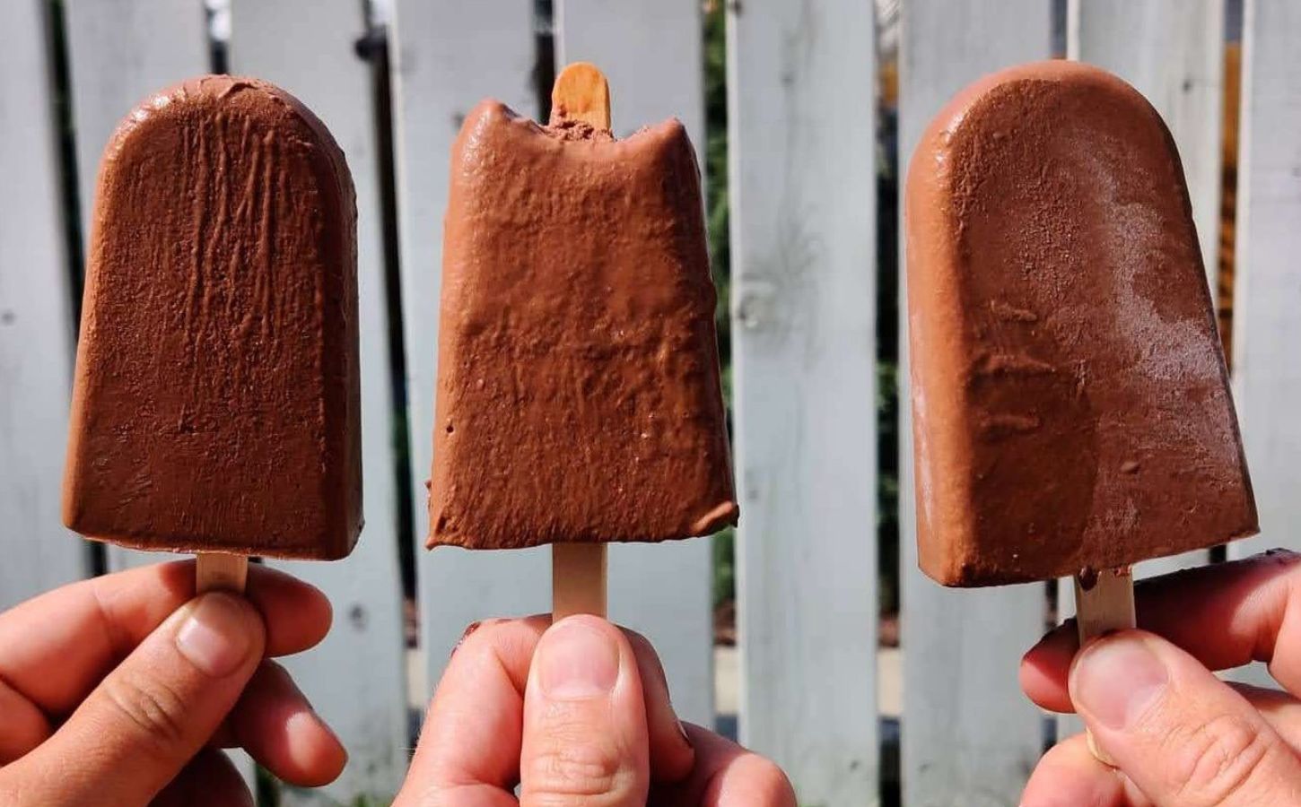 a picture of three vegan chocolate banana popsicles made with coconut milk, cocoa powder, banana, and maple syrup