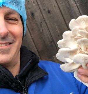 Photo shows chef Derek Sarno wearing PPE and holding up a handful of bright white, layered mushrooms to the camera