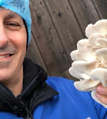 Photo shows chef Derek Sarno wearing PPE and holding up a handful of bright white, layered mushrooms to the camera