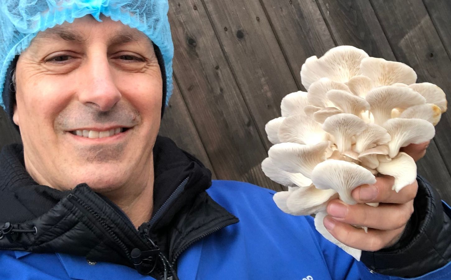 Photo shows chef Derek Sarno wearing PPE and holding up a handful of bright white, layered mushrooms to the camera