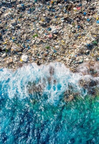 A blue wave washing up on a beach full of plastic pollution