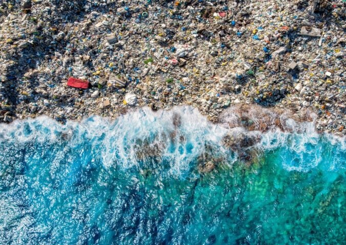 A blue wave washing up on a beach full of plastic pollution