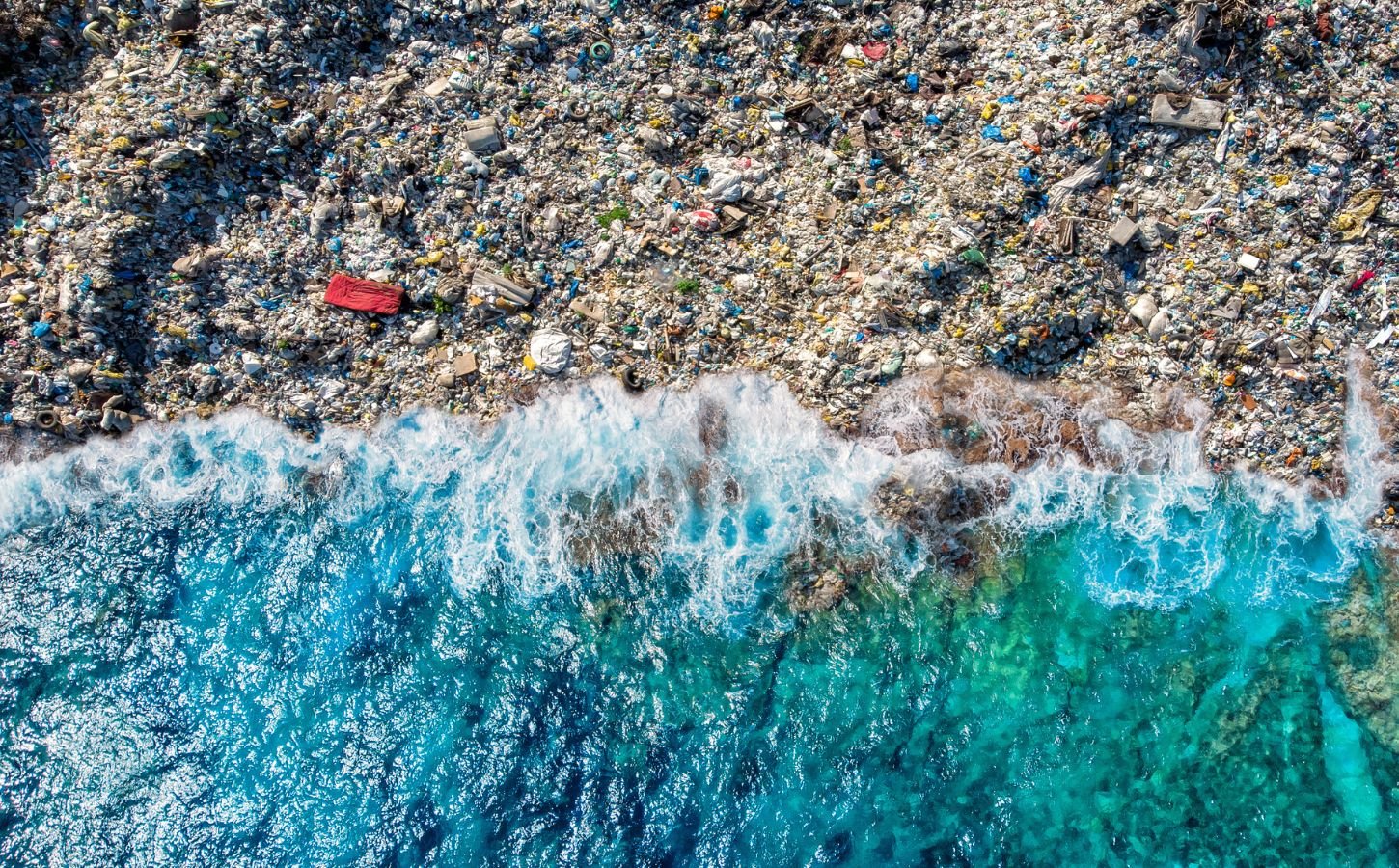 A blue wave washing up on a beach full of plastic pollution