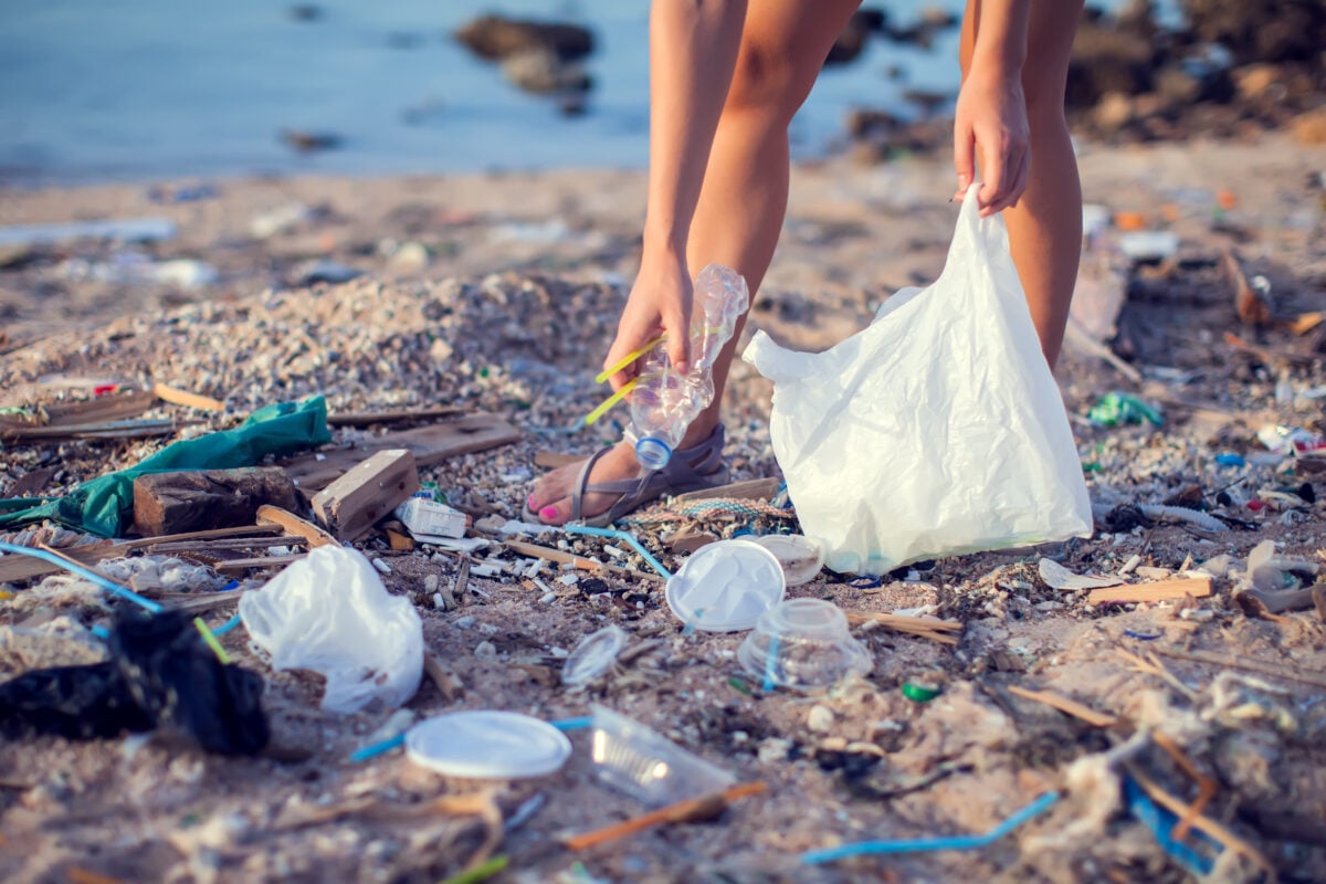 A person picking up plastic bottles and other rubbish from a beach