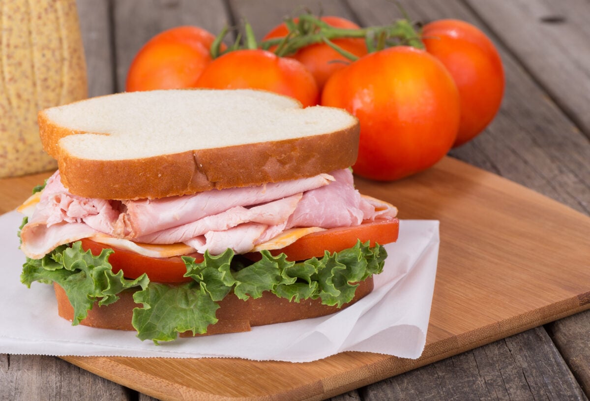 A ham sandwich with cheese, lettuce, and tomato next to some tomatoes