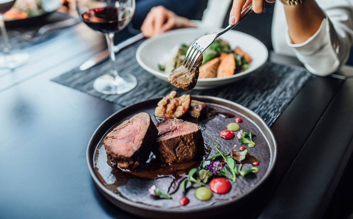 A woman eating a steak in a restaurant with a glass of wine