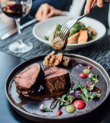 A woman eating a steak in a restaurant with a glass of wine