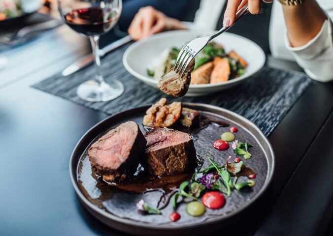 A woman eating a steak in a restaurant with a glass of wine