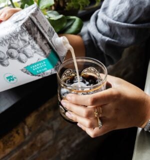 Photo shows someone pouring Milkadamia macadamia milk into a cup of coffee. The brand's new product is "2D printed" oat milk.